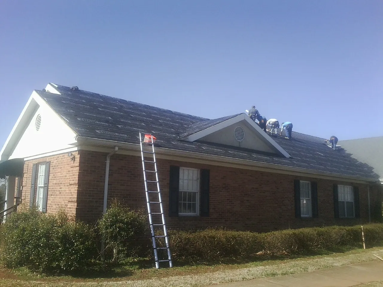 Crew tearing shingles off a brick ranch roof with a ladder set — Metal Roof Repair work by our crew in Buchanan