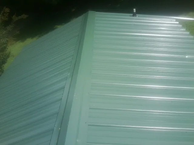 New green metal panels meeting at the ridge of a roof — Flat Roof Repair work by our crew in Buchanan